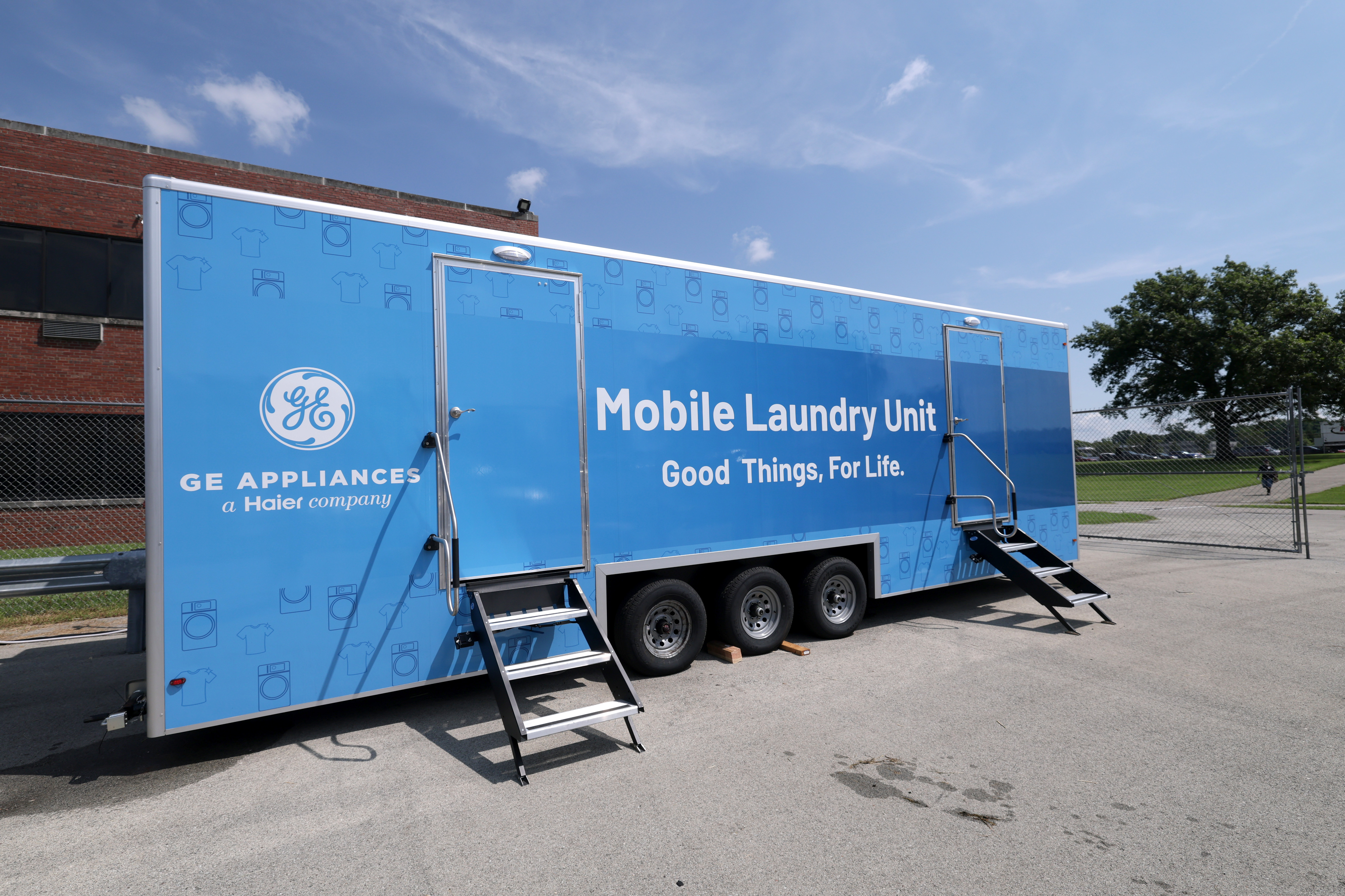 A blue tractor trailor sits outside Appliance Park wrapped in branding that reads the GE Appliances logo and the title "Mobile Laundry Unit. Good things, for life". 