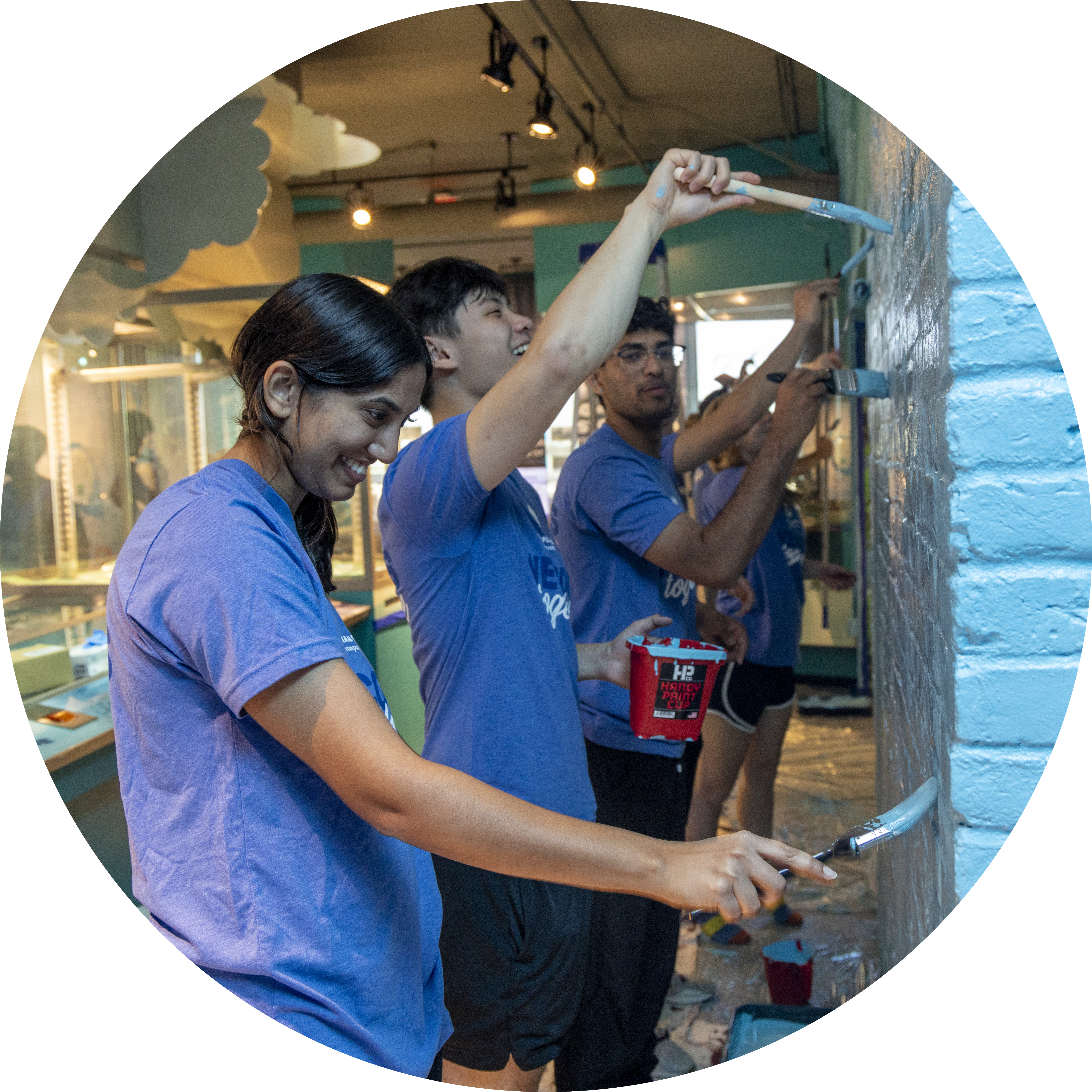 A young woman and man are smiling as they stand side by side painting blue on a brick wall during the 2025 Blue Wave community event
