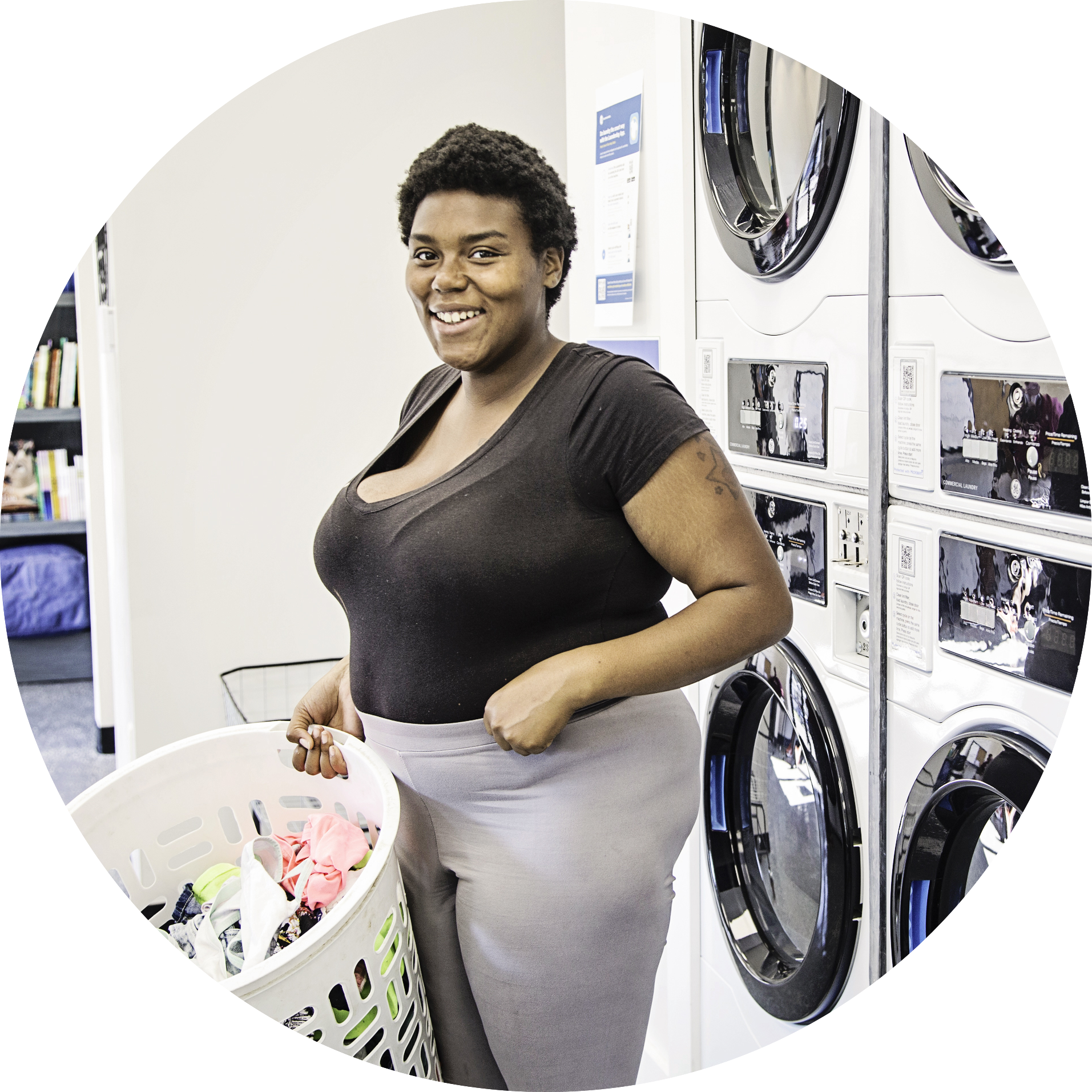 A woman smiles at the camera in front of several stacked GE Appliances washers and dryers as part of the new Smoketown laundry service opening